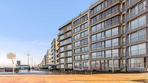 Un immeuble résidentiel à plusieurs étages, doté de balcons, d’un espace de stationnement et surplombant un ciel dégagé.