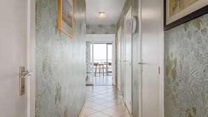 Un couloir avec un papier peint à motifs, un sol carrelé et une porte donnant sur un coin repas.