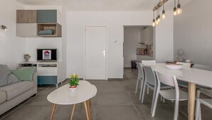 Moderni olohuone, jossa on sohva, ruokapöytä tuoleineen, televisio ja pieni kasvi valkoisella pöydällä.