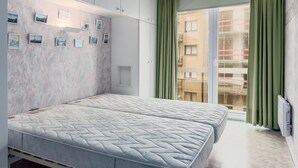 Een slaapkamer met een bed, een kledingkast, een wandplank met foto’s en een schuifdeur naar buiten.