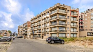 Een meerlaags woongebouw met balkons, een verharde weg, geparkeerde auto's en een heldere lucht.