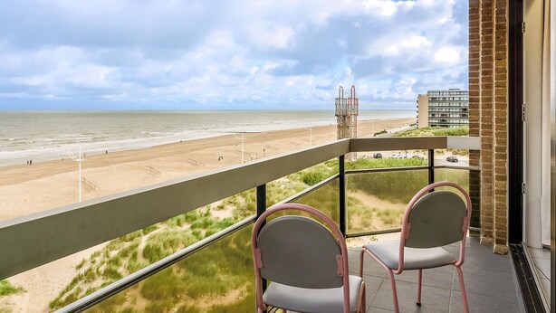 Een balkon met twee stoelen met uitzicht op een strand en een gebouw in de verte.