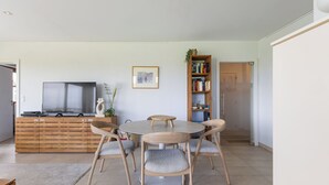 A modern living room with a round wooden table, four matching chairs, a flat-screen TV, a bookshelf, and a framed picture on the wall. - Zonnehaven II E 0209+G47* (NIEUWPOORT)