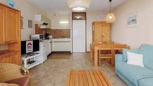 Een ruimtelijk ingedeelde leefruimte met kitchenette, een eethoek en een zithoek met een bank en stoelen.