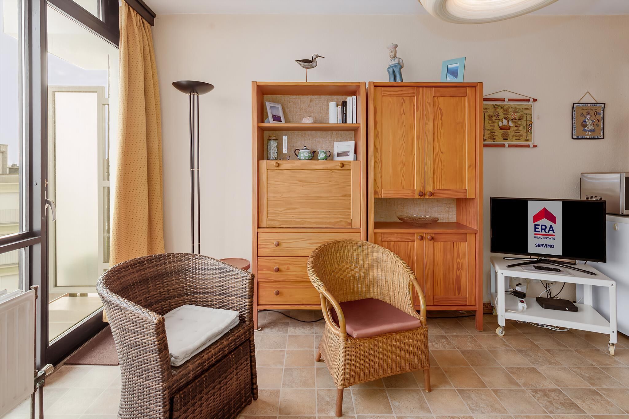A room with wicker chairs, a wooden cabinet, a television, and a floor lamp.