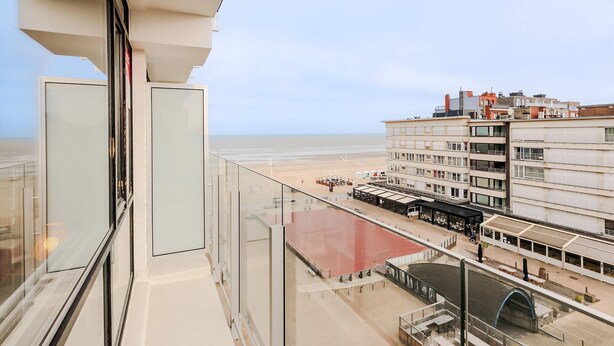 Een hoog hotel met een glazen balkon met uitzicht op een strand en omliggende gebouwen.