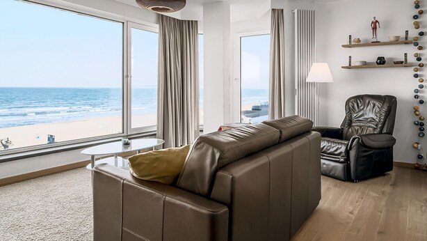 A modern living room with a leather sofa, a black leather chair, and a view of the beach. - Idesende 2/0203 + P* (Sint Idesbald)