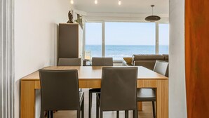 A modern dining area with a wooden table and chairs, a sofa, and a view of the sea through large windows. - Idesende 2/0203 + P* (Sint Idesbald)