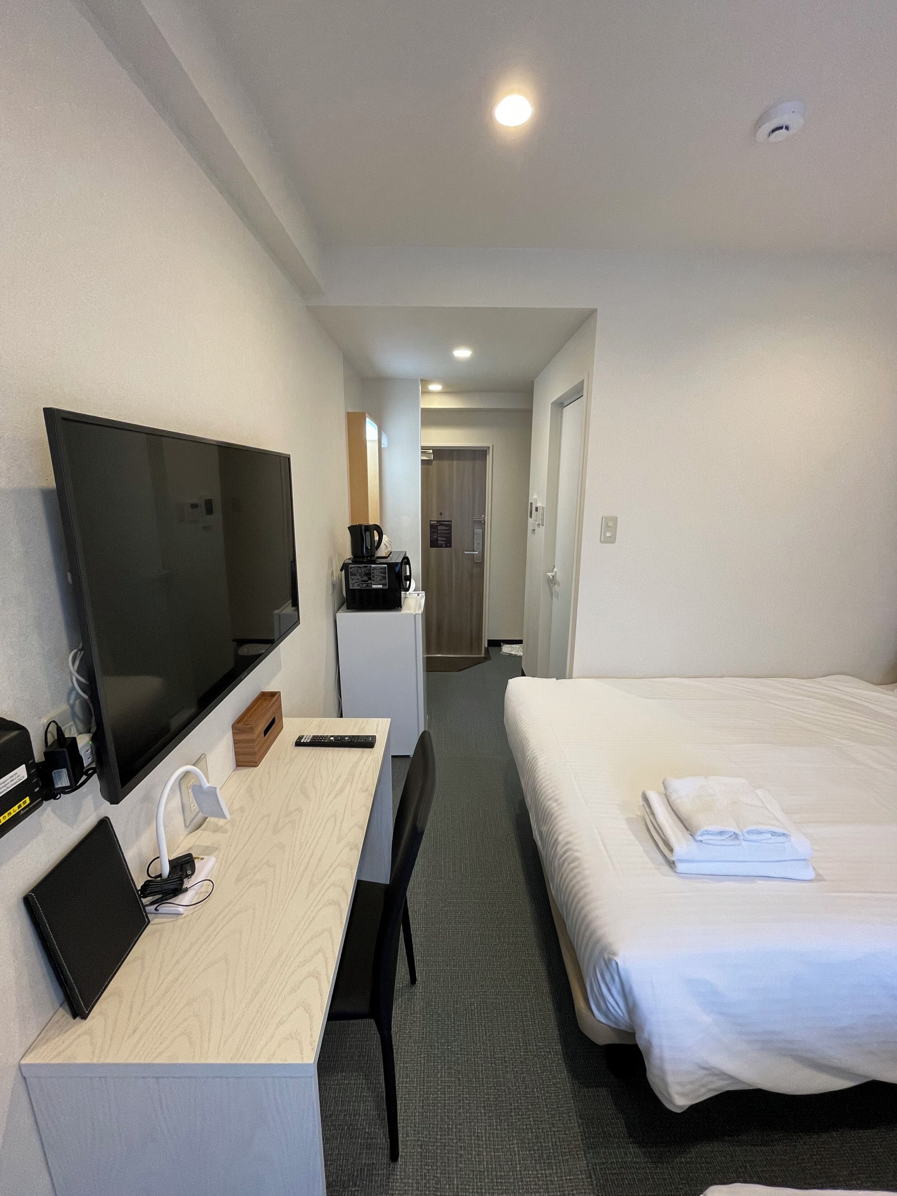 Habitació d'hotel amb llit, escriptori amb televisió, màquina de cafè i porta que dona a un bany.