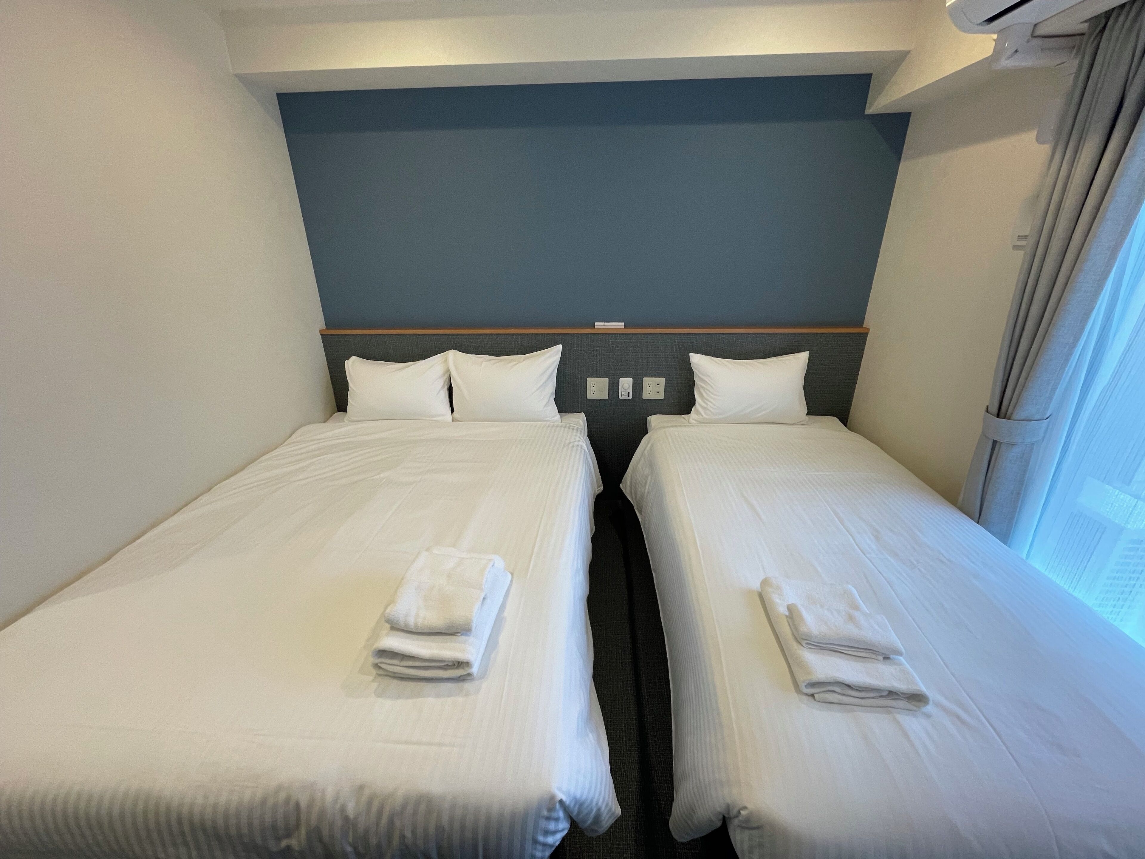 A hotel room with two single beds, each with a neatly folded towel.