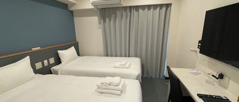 A hotel room with two beds, a desk, a TV, and an air conditioning unit.