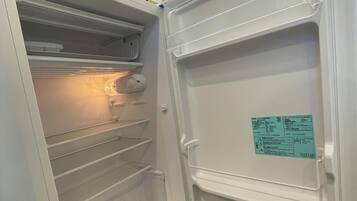 Un réfrigérateur ouvert, avec des étagères transparentes et un autocollant sur la porte.