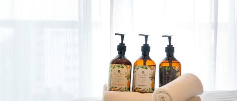 A bed with a rolled towel and three bottles of Orange Rose Beaute products on a white bedspread.