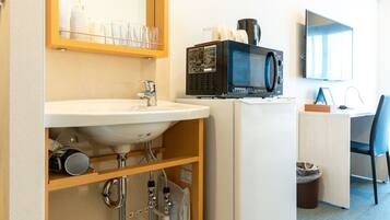 Habitación de hotel compacta con lavabo, espejo, microondas y un pequeño escritorio con silla.