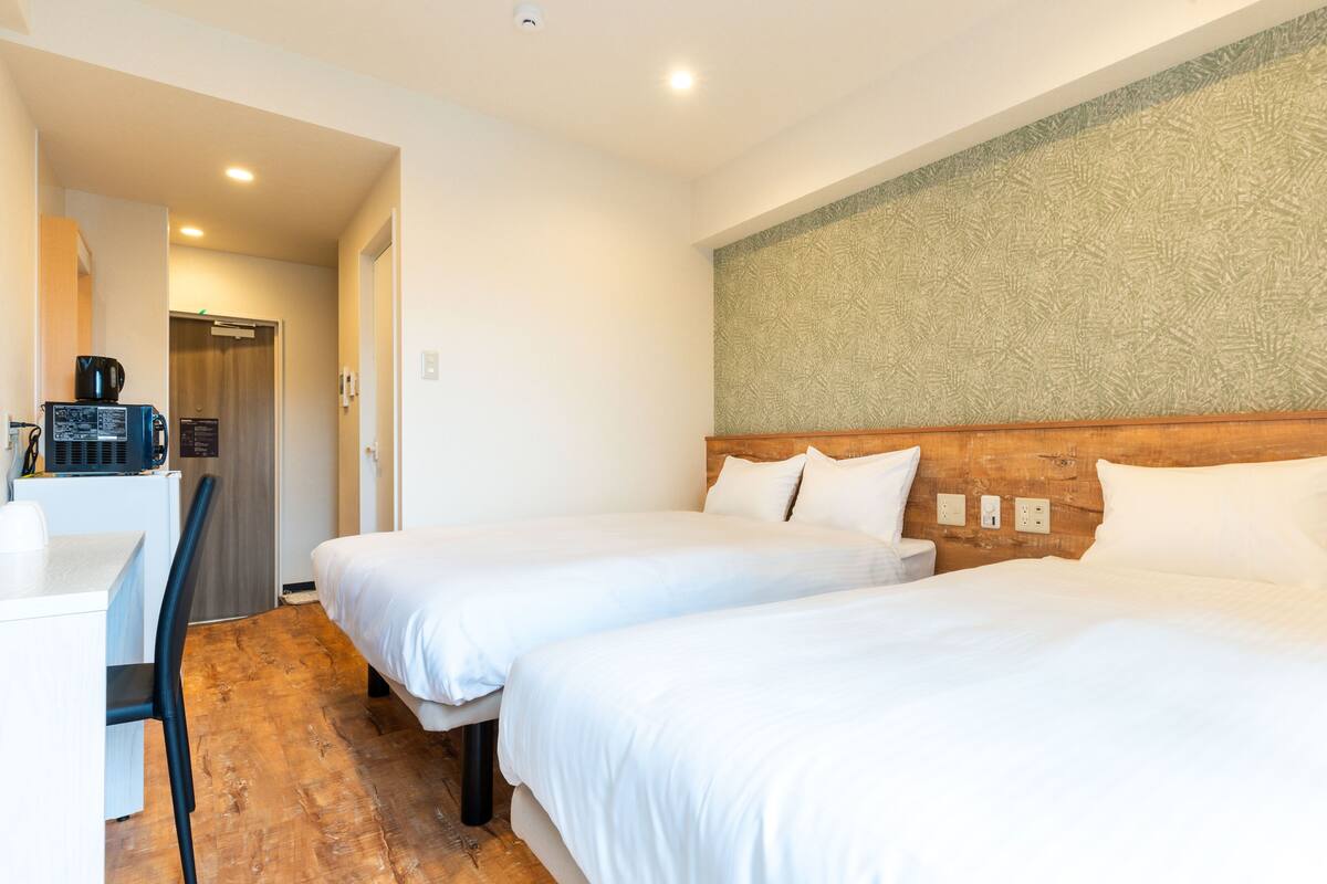Une chambre d’hôtel avec deux lits, un bureau, une chaise et un four à micro-ondes.