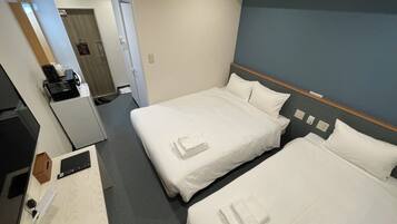 Habitación de hotel con dos camas, un escritorio con ordenador, una cafetera y un espejo.