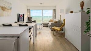 Un salon moderne comprenant un canapé, des fauteuils, une table à manger et offrant une vue sur la mer grâce à de grandes fenêtres.