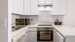 Une cuisine moderne avec des meubles blancs, une cuisinière en acier inoxydable, un four, un lave-vaisselle et un micro-ondes encastré.