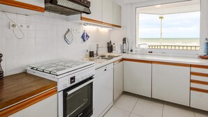 Cocina moderna con armarios blancos, estufa a gas, horno empotrado, lavamanos y ventana con vista al mar.