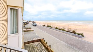 Una calle costera con acera pavimentada, una playa al fondo y un edificio con ventana y puerta.