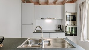 Une cuisine moderne dotée d’un évier en acier inoxydable, de meubles blancs et d’appareils électroménagers intégrés, notamment un four et un four à micro-ondes.