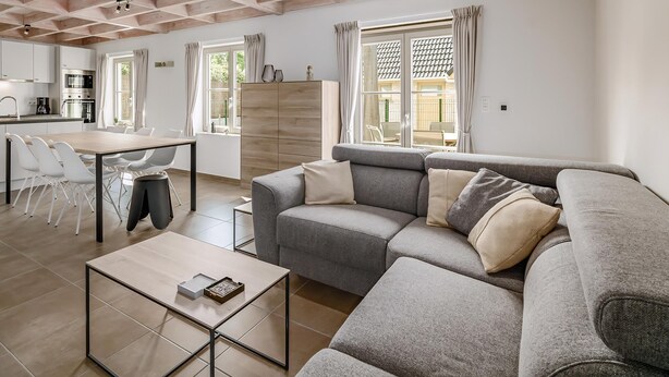 Un salon moderne avec un canapé gris, une table basse en bois et un coin repas comprenant une table et des chaises blanches.