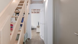 Un couloir étroit, avec un escalier en bois sur la gauche, qui mène à une pièce comprenant un lit et un bureau.