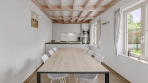 Une cuisine moderne avec des meubles blancs, une table à manger en bois et une grande fenêtre agrémentée de rideaux.