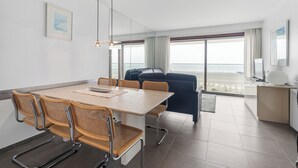 Une chambre d’hôtel moderne dotée d’un coin repas, d’un canapé, d’un bureau et de grandes fenêtres offrant une vue dégagée.