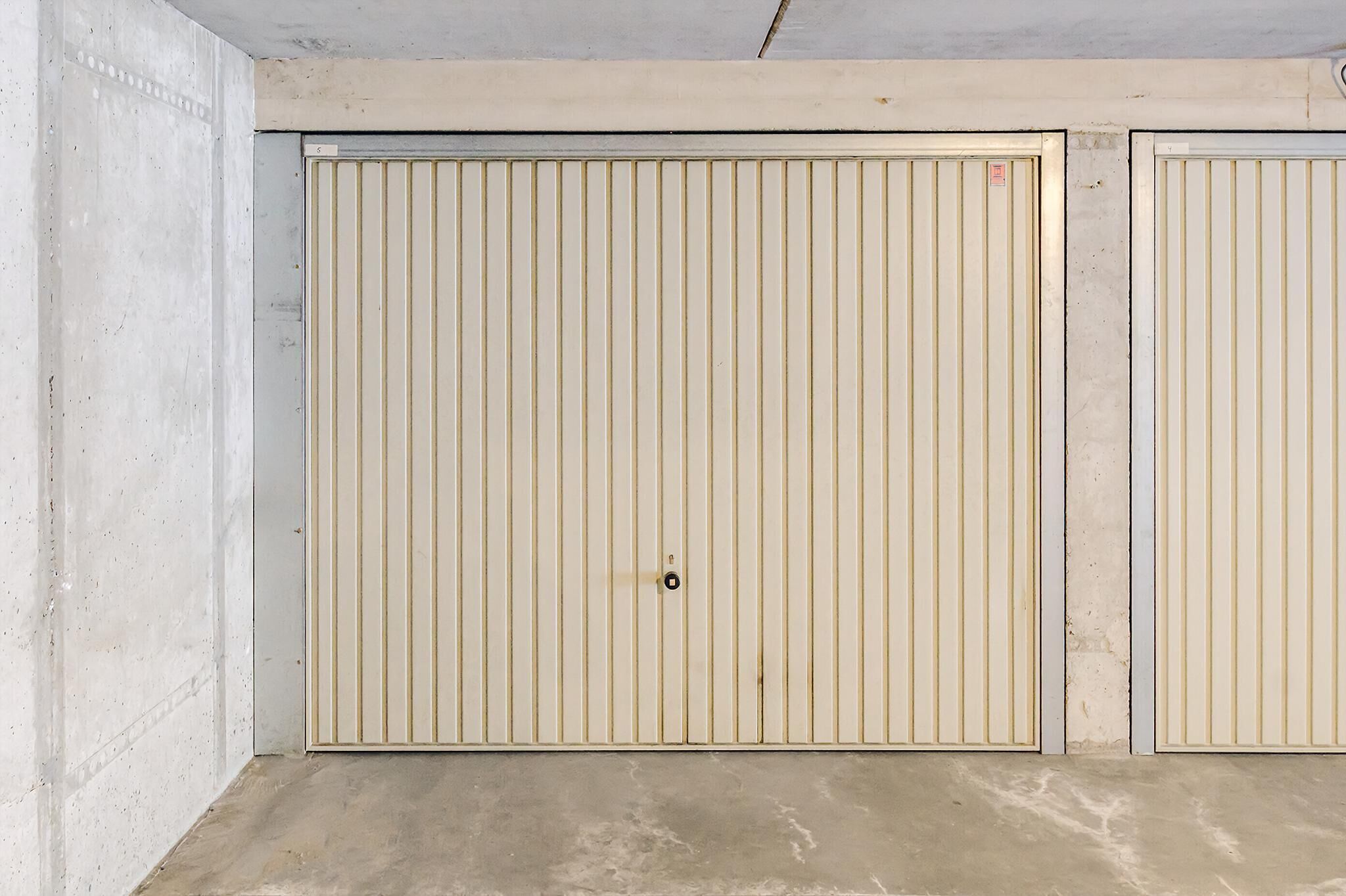 Eine geschlossene, beige-farbene Tür mit vertikalen Streifen in einem Raum mit Betonwänden und -boden.