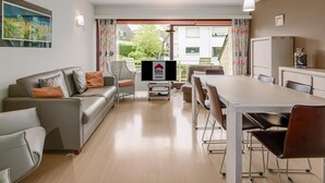 Ein modernes Wohnzimmer mit einer Couch, Sesseln, einem Esstisch und einem Fernseher.