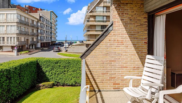 Ein Balkon mit einem weißen Stuhl, einer Backsteinmauer und Blick auf eine Straße mit Autos und Gebäuden.