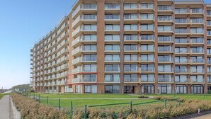 A multi-story hotel with a modern design, featuring balconies on each floor, a central entrance, and a well-maintained lawn area. - Den Oever V 0106 met parking (Nieuwpoort)
