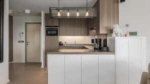 A modern kitchen with white cabinetry, a central island, and pendant lighting. - Den Oever V 0106 met parking (Nieuwpoort)