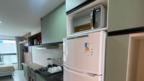 A modern kitchen with a white refrigerator, a stove, and a microwave. There is a dining area with a table and chairs. - Villas do Porto - 108 by La Playa (Ipojuca)