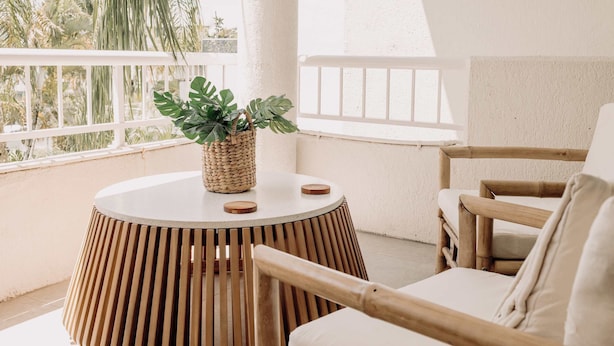 A round wooden table with a woven plant holder, a white cushioned chair, and a view of palm trees through a balcony railing. - Headlands Beachside Gem - 50mtrs To Toes In Sand! (Alexandra Headland)