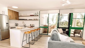 A modern kitchen with a central island, bar stools, and a dining area with a view of the outdoors. - Headlands Beachside Gem - 50mtrs To Toes In Sand! (Alexandra Headland)