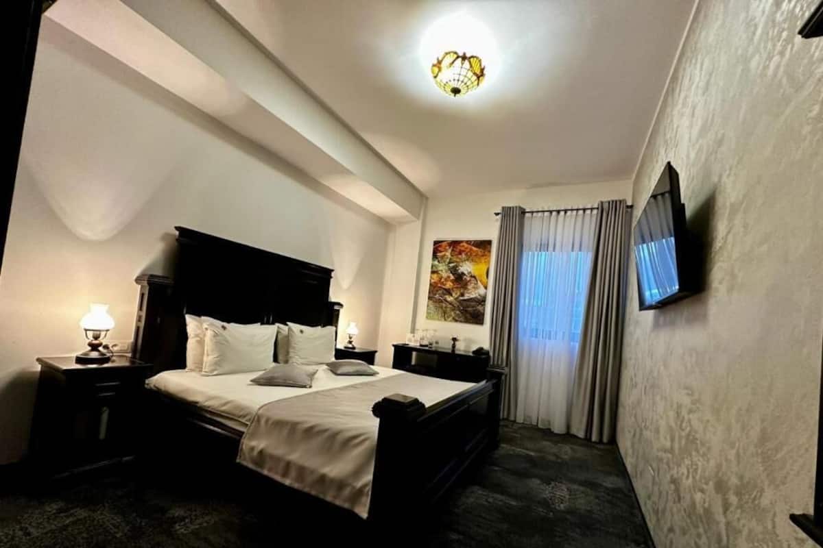 Quarto de hotel com cama, mesas de cabeceira, televisão na parede e um quadro na parede.