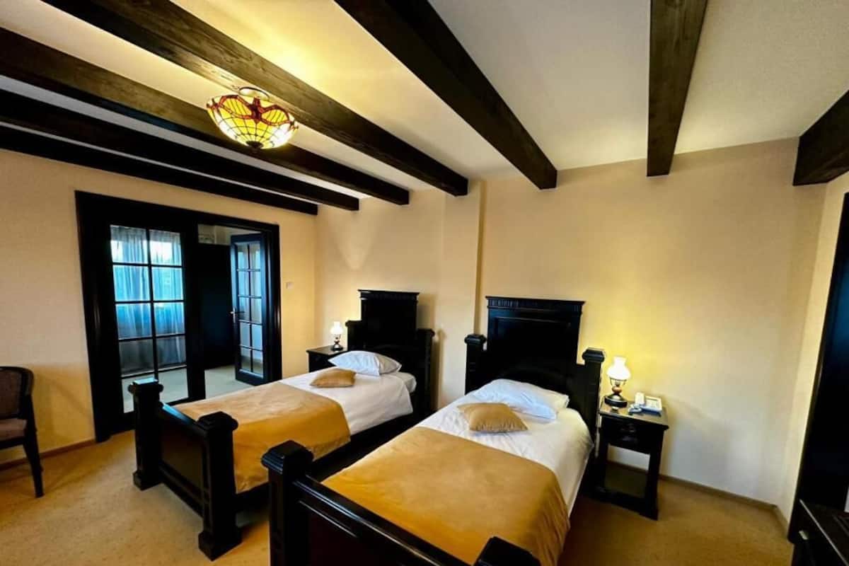 Quarto com duas camas, cabeceiras de madeira, um candelabro e uma pequena mesa com abajur.