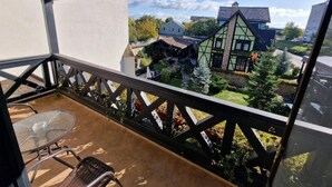 Un balcón con una mesa y sillas de vidrio, con vista a una casa tradicional de fachada verde y tejado inclinado.