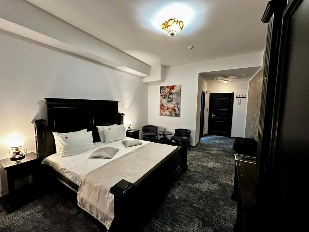 A hotel room with a large bed, a nightstand with a lamp, a painting on the wall, and a carpeted floor.