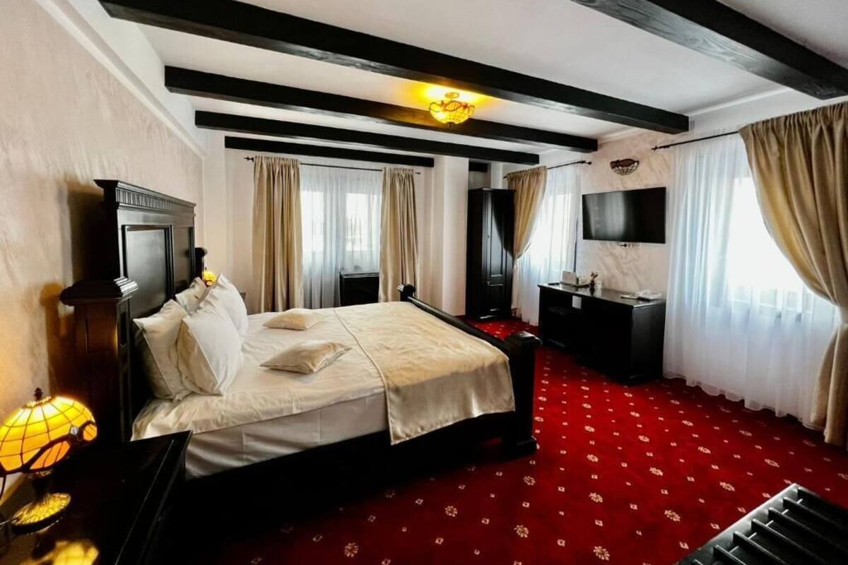 Quarto de hotel com uma cama, uma escrivaninha, uma televisão e um tapete vermelho.