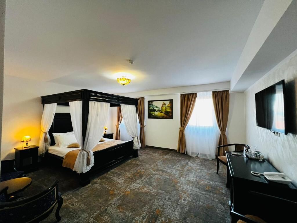 Quarto de hotel com cama de dossel, escrivaninha, cadeira, televisão e um quadro na parede.