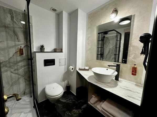 A modern bathroom with a marble shower, a white toilet, a large mirror, and a white sink.