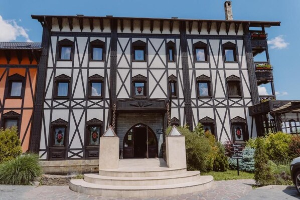 A traditional half-timbered building with a central entrance, a stone staircase leading up to it, and a sign indicating a restaurant. - Podu' Cu Lanturi  (Bacau)