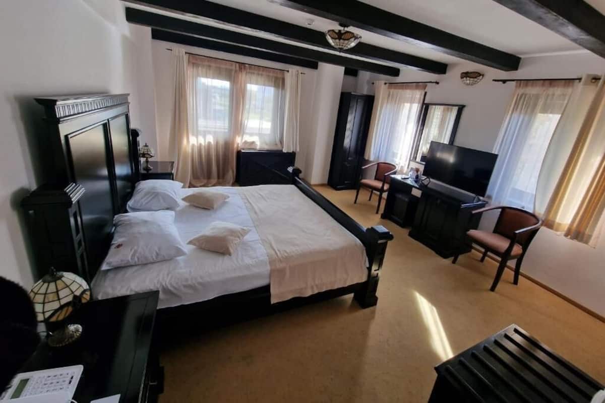 Quarto de hotel com cama, escrivaninha, cadeira, televisão e janela com cortinas.