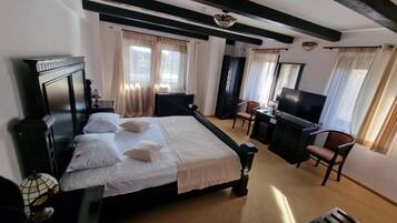 Ein Hotelzimmer mit Bett, Schreibtisch, Stuhl, Fernseher und einem Fenster mit Vorhängen.