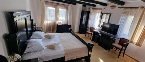 A hotel room with a bed, a desk, a chair, a television, and a window with curtains.