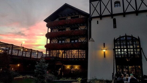 Un edificio de estilo arquitectónico tradicional, con un balcón adornado con flores rojas, una entrada bien iluminada y un jardín con fardos de heno y calabazas.