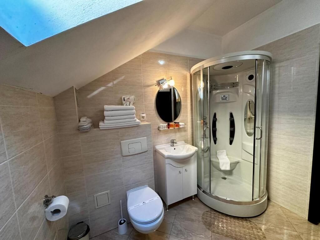 Ein modernes Badezimmer mit einer gläsernen Duschkabine, Toilette, Waschbecken und einem Oberlicht.